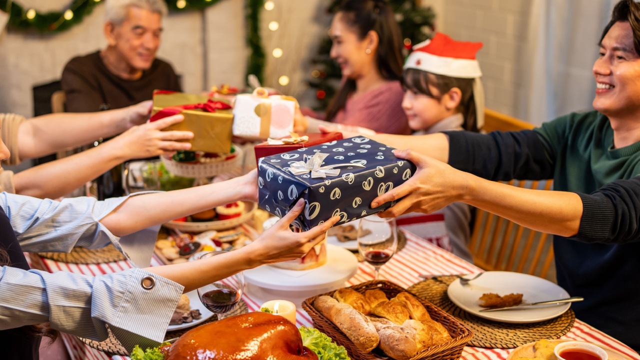 Asian lovely family exchanging presents during Christmas party at home. Group of attractive people receiving gift box from each other while having dinner celebrate holiday Thanksgiving on dining table