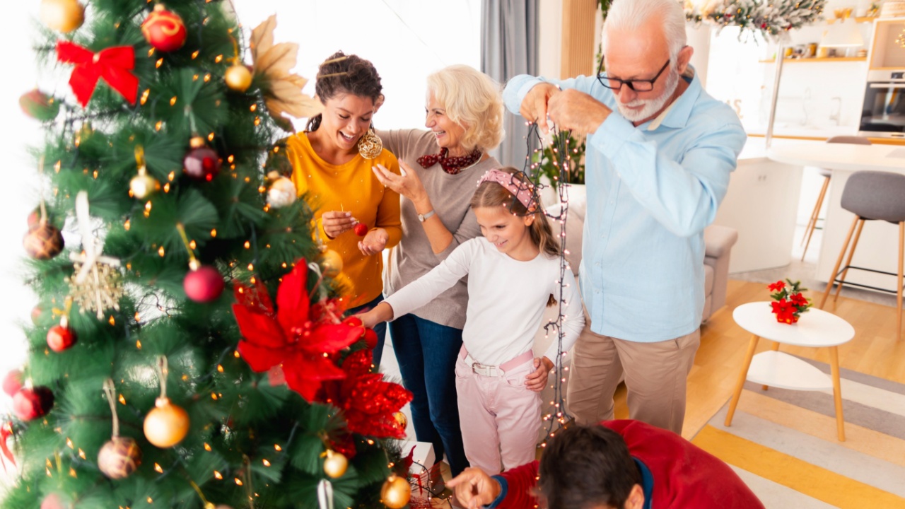 Beautiful happy multi-generation family gathered at home for winter holiday season celebration having fun decorating Christmas tree