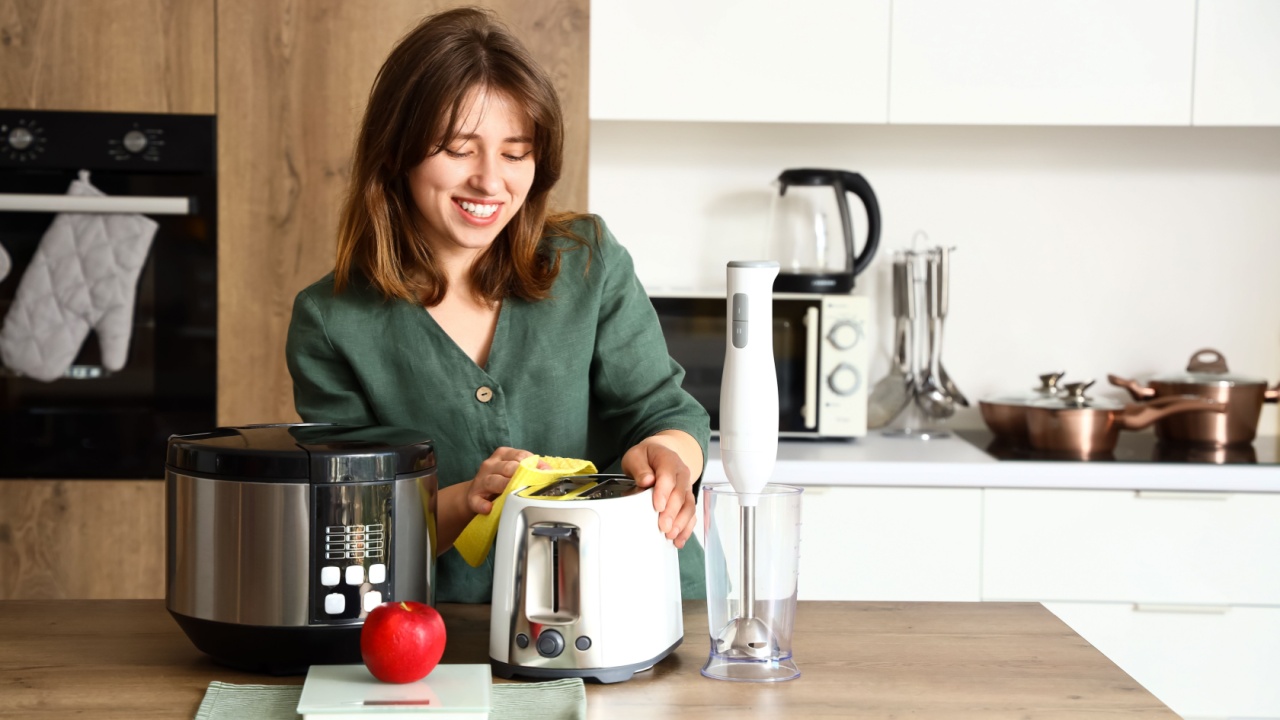 Young woman cleaning electric toaster in light kitchen