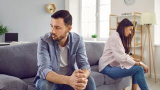 Disappointed couple sitting on sofa back to back, facing away from each other. Portrait of frustrated husband and wife feeling upset after argument and making decision of breaking up get divorced