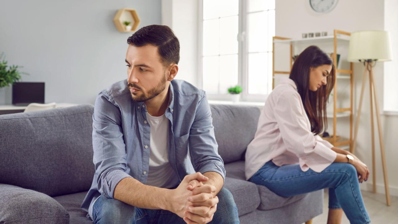 Disappointed couple sitting on sofa back to back, facing away from each other. Portrait of frustrated husband and wife feeling upset after argument and making decision of breaking up get divorced