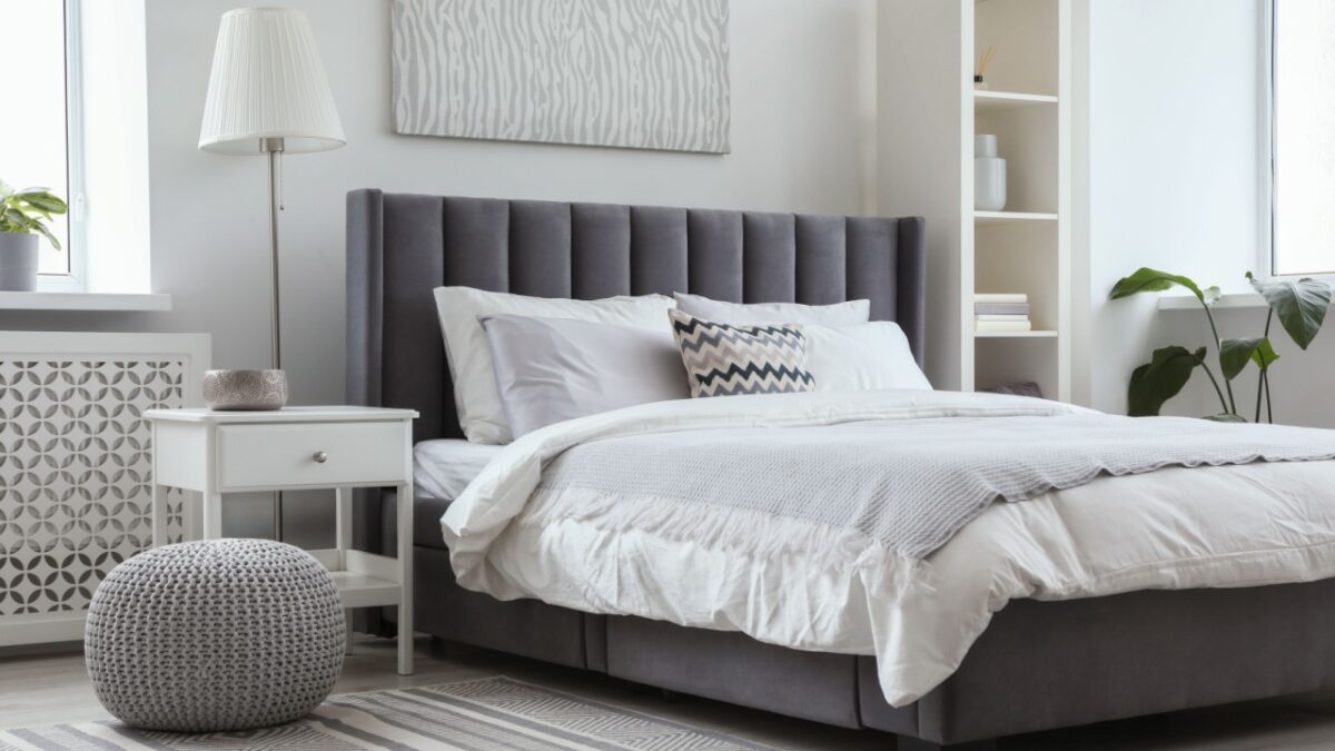 Stylish light bedroom interior with large comfortable bed, shelving unit and bedside table