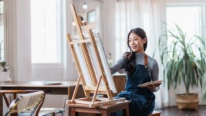 Happy asian woman artist drawing picture on canvas in studio.
