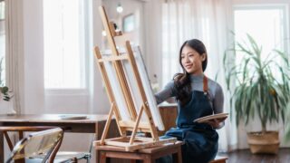 Happy asian woman artist drawing picture on canvas in studio.