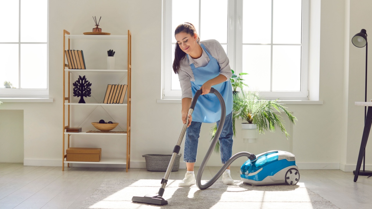Full length portrait, of a woman dedicated to the art of cleaning home or house hold service. With a vacuum in hand, she transforms living room, meticulously vacuuming the carpet at floor.