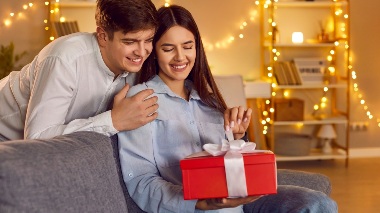 Happy people in love close holding red gift box, enjoy romantic moment. Valentine day emotion, loving male, female pair young couple celebrate romance, enjoy intimacy, room garland interior design