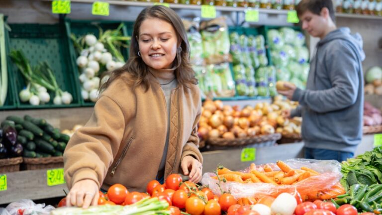 Young female shopper selects and buys tomatoes in a supermarket