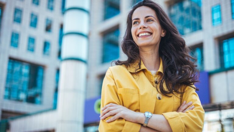 Portrait of a beautiful happy woman outdoors. Smiling woman in the city. Candid portrait of a cheerful young woman wearing an yellow shirt spending time in the city.
