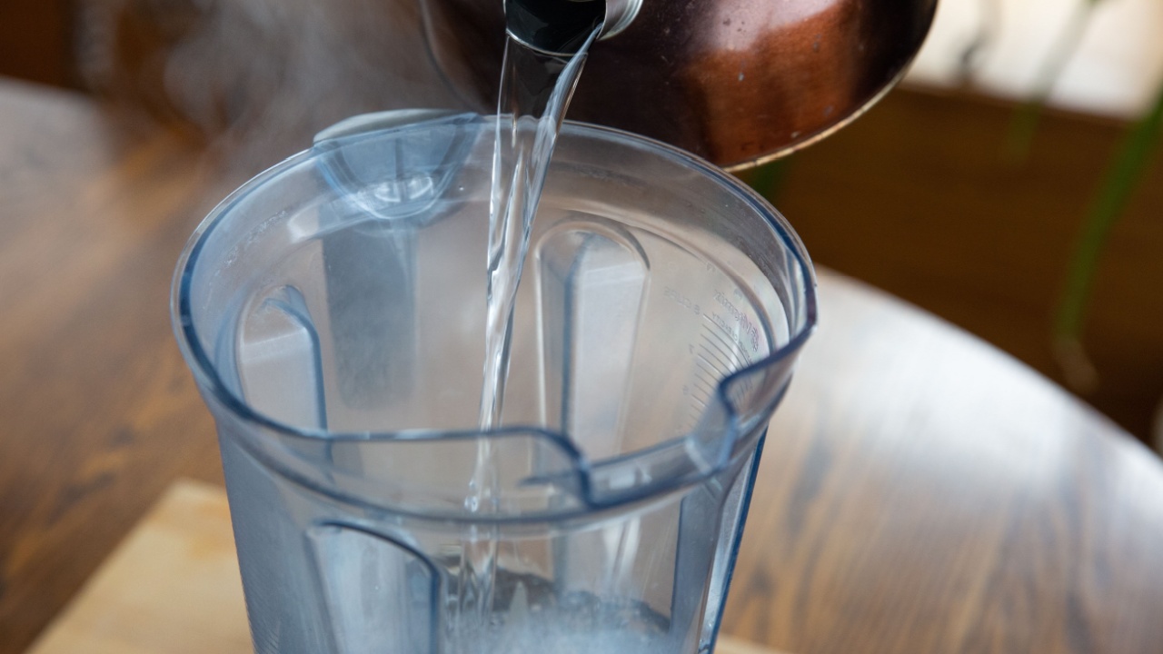 Hot water being poured from tea kettle into blender. 
