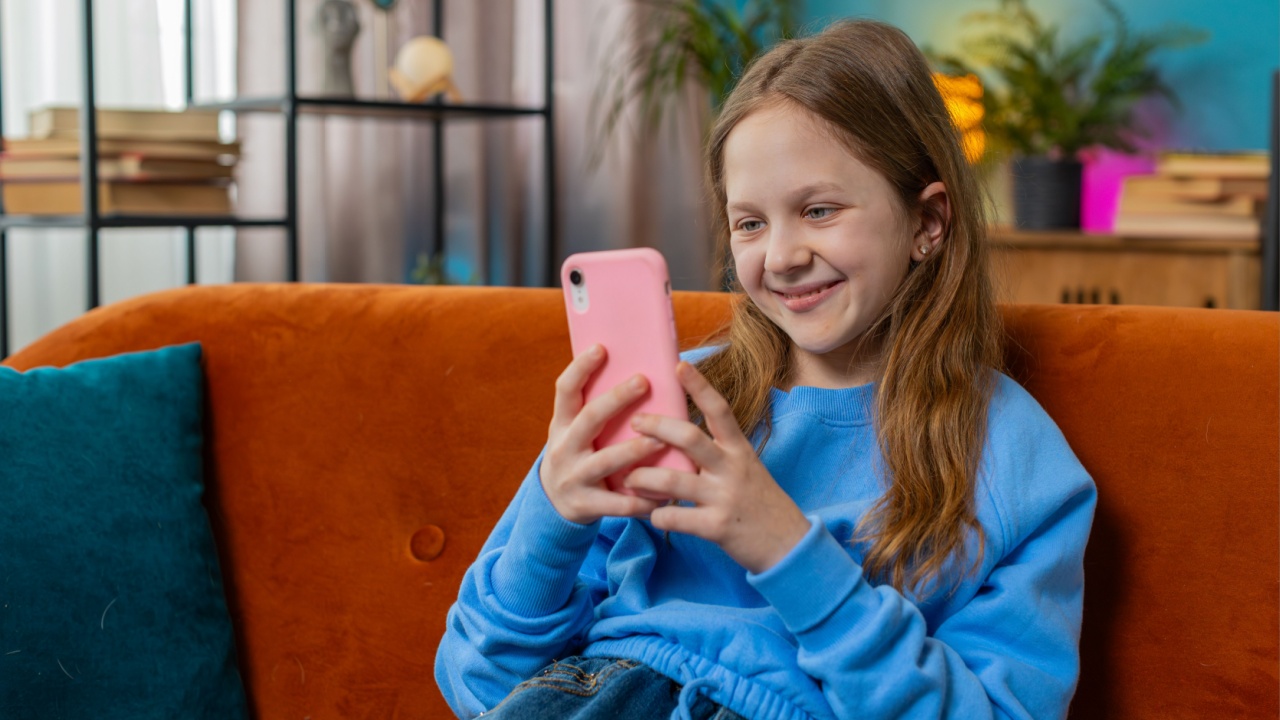 Cheerful preteen girl texting share messages on smartphone social media applications online watching relax movie. Female Caucasian teenager kid using mobile phone at home in living room sits on sofa.