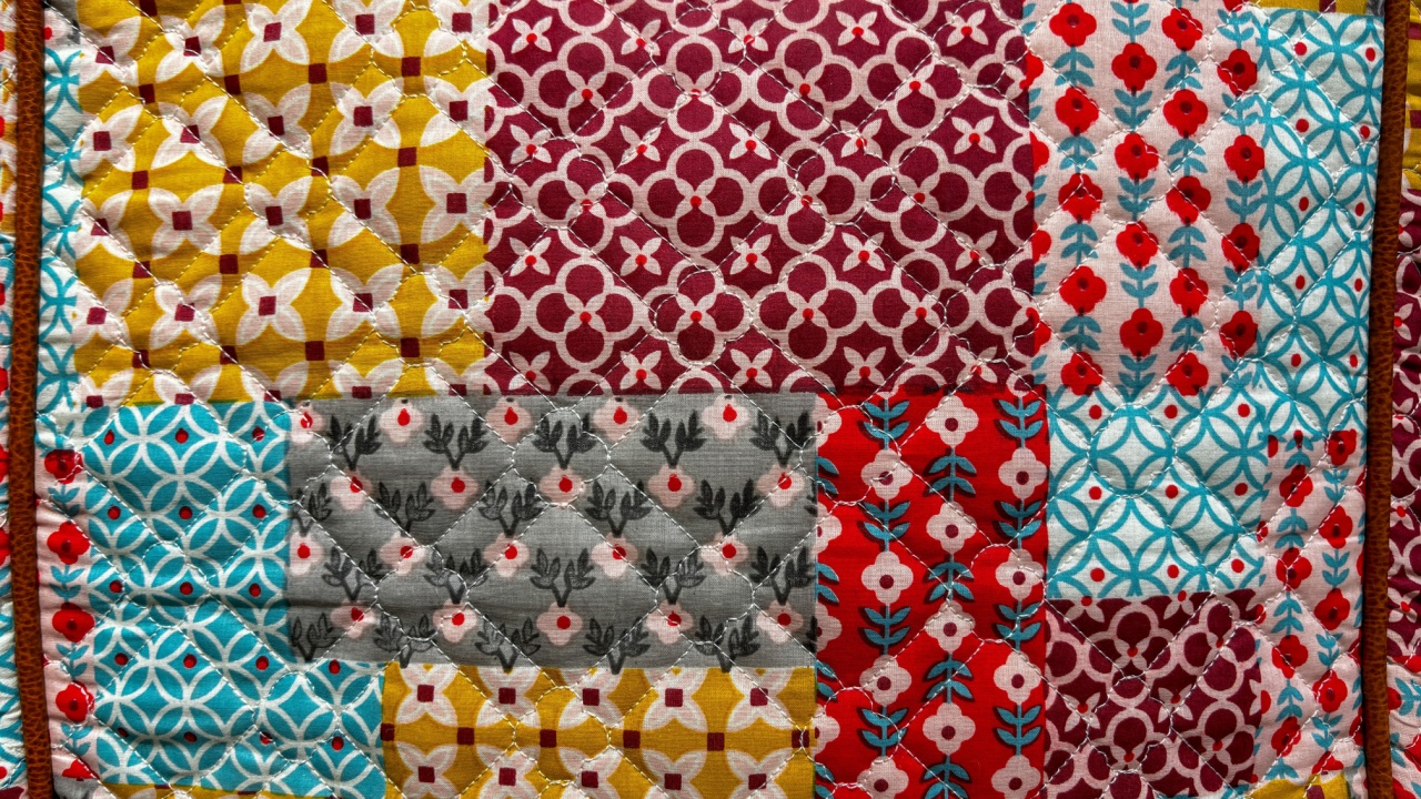 A colorful quilt with a variety of patterns and colors. The quilt is made up of different pieces of fabric, and it is a patchwork quilt. Scene is cheerful and vibrant