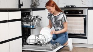 Smiling woman loading dishwasher with plates in kitchen