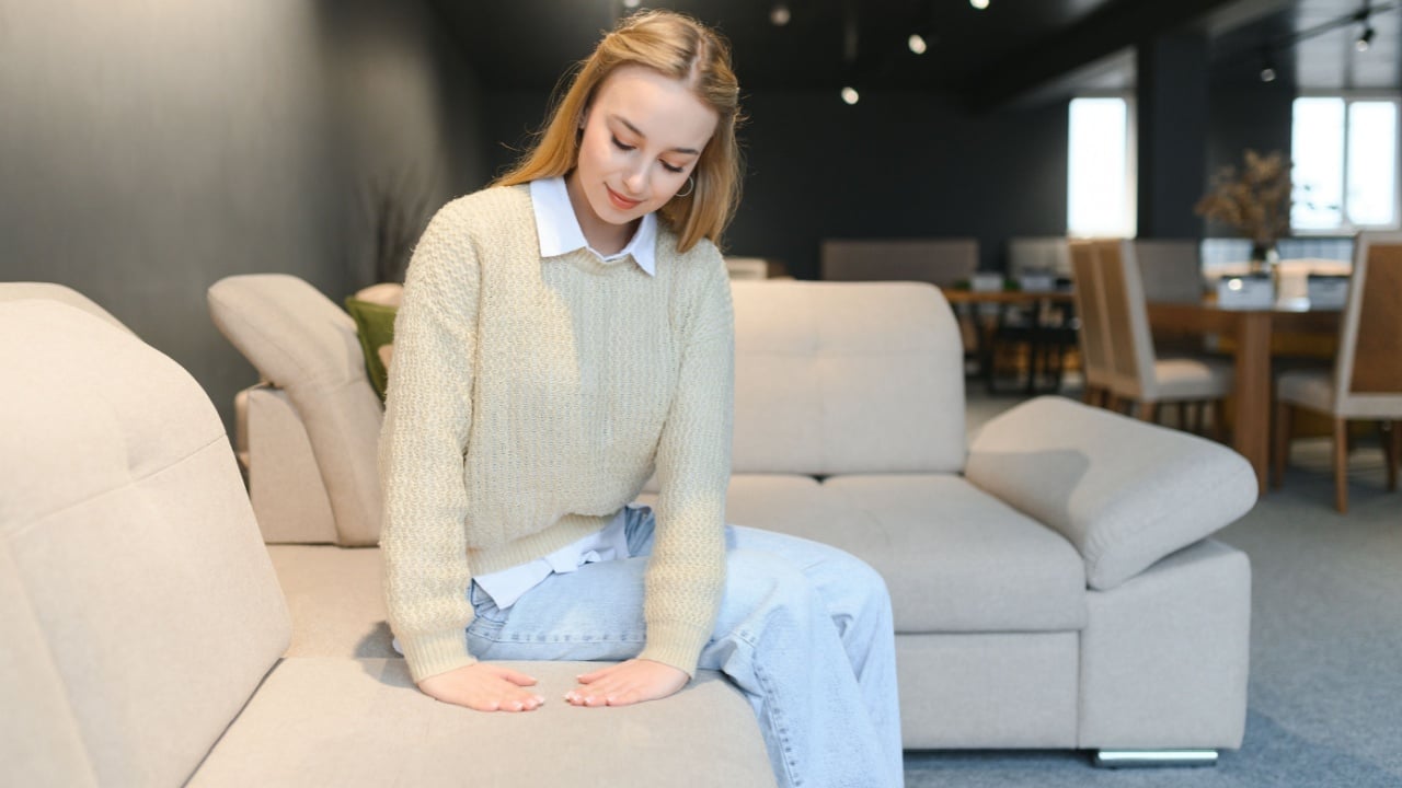 Portrait of young cheerful woman testing sofa in furniture store.