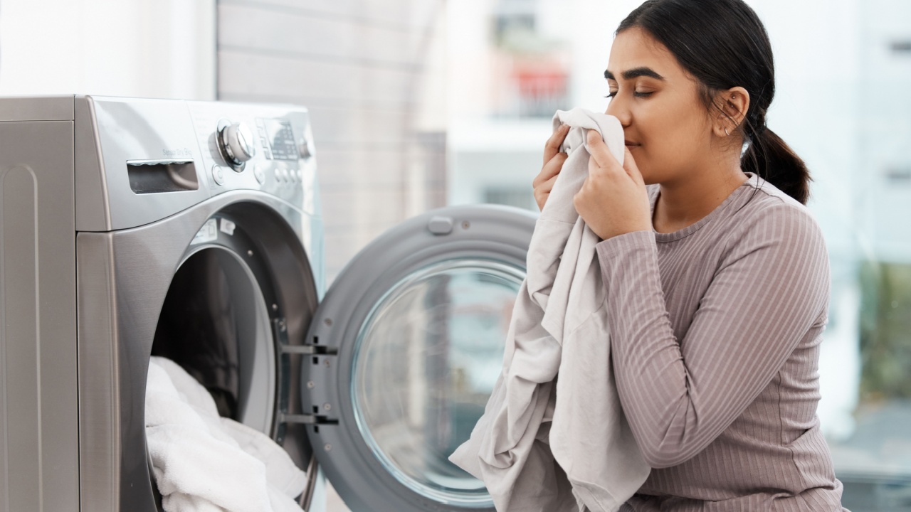 Laundry, fresh scent and washing machine with woman smelling clothes in home for spring cleaning. Aroma, fabric and housework with person in apartment for domestic chores or weekend housekeeping
