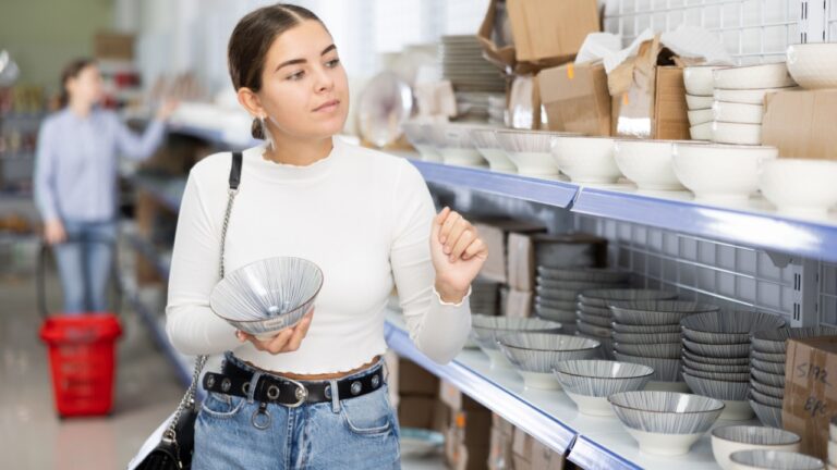 Young woman in supermarket is choosing plates. Female buyer examines ceramic kitchen utensils with