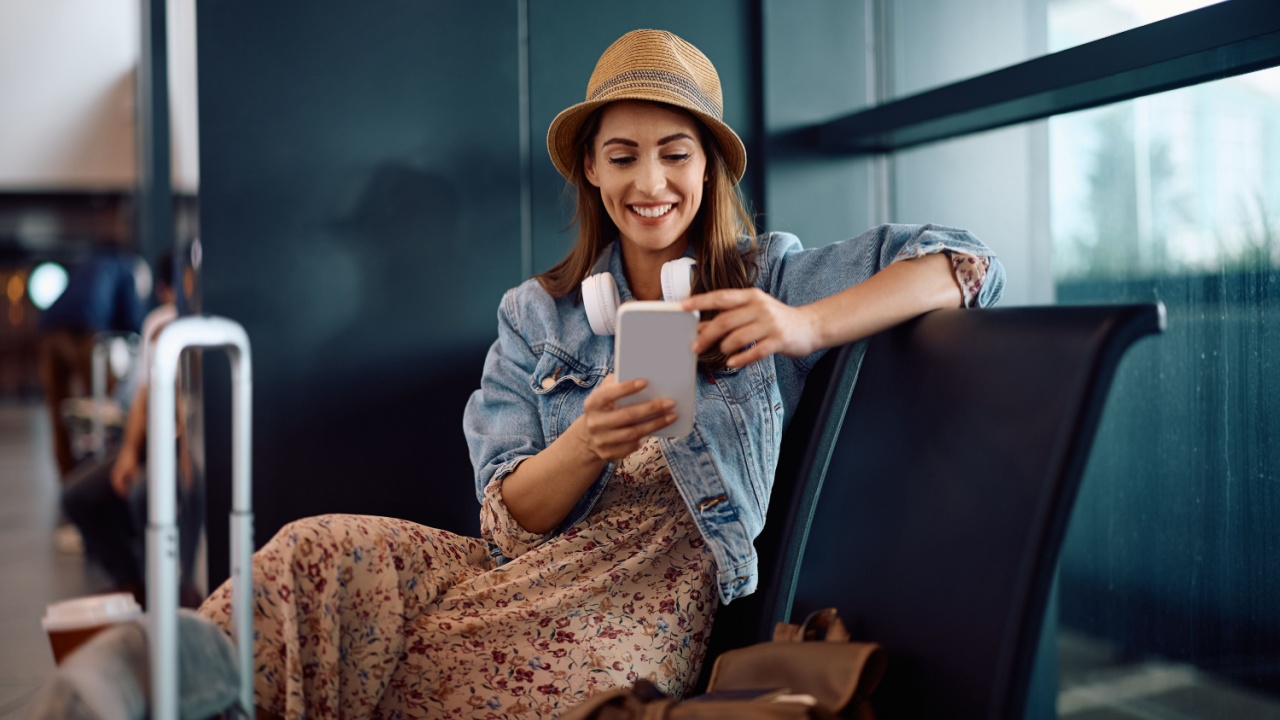 Happy woman using smart phone while waiting for her flight at departure area.