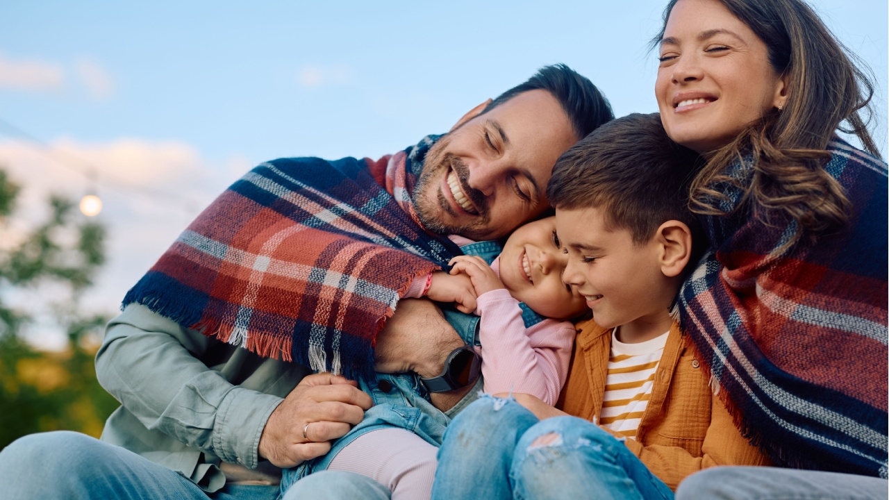 Happy parents and their children relaxing outdoors while being wrapped in a blanket. 