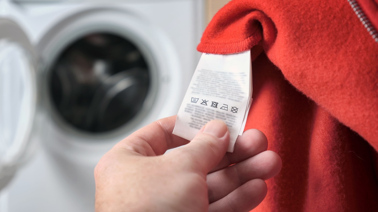 A man checking information the label on a red sports jacket, with a washing machine in the background. Clothes care and washing rules. Selective focus.
