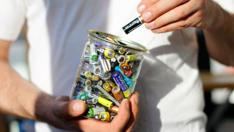 Russia, Saint Petersburg May 20, 2024: The hand putting used batteries into jar for recycling. Concept of collection batteries for recycling and separating waste