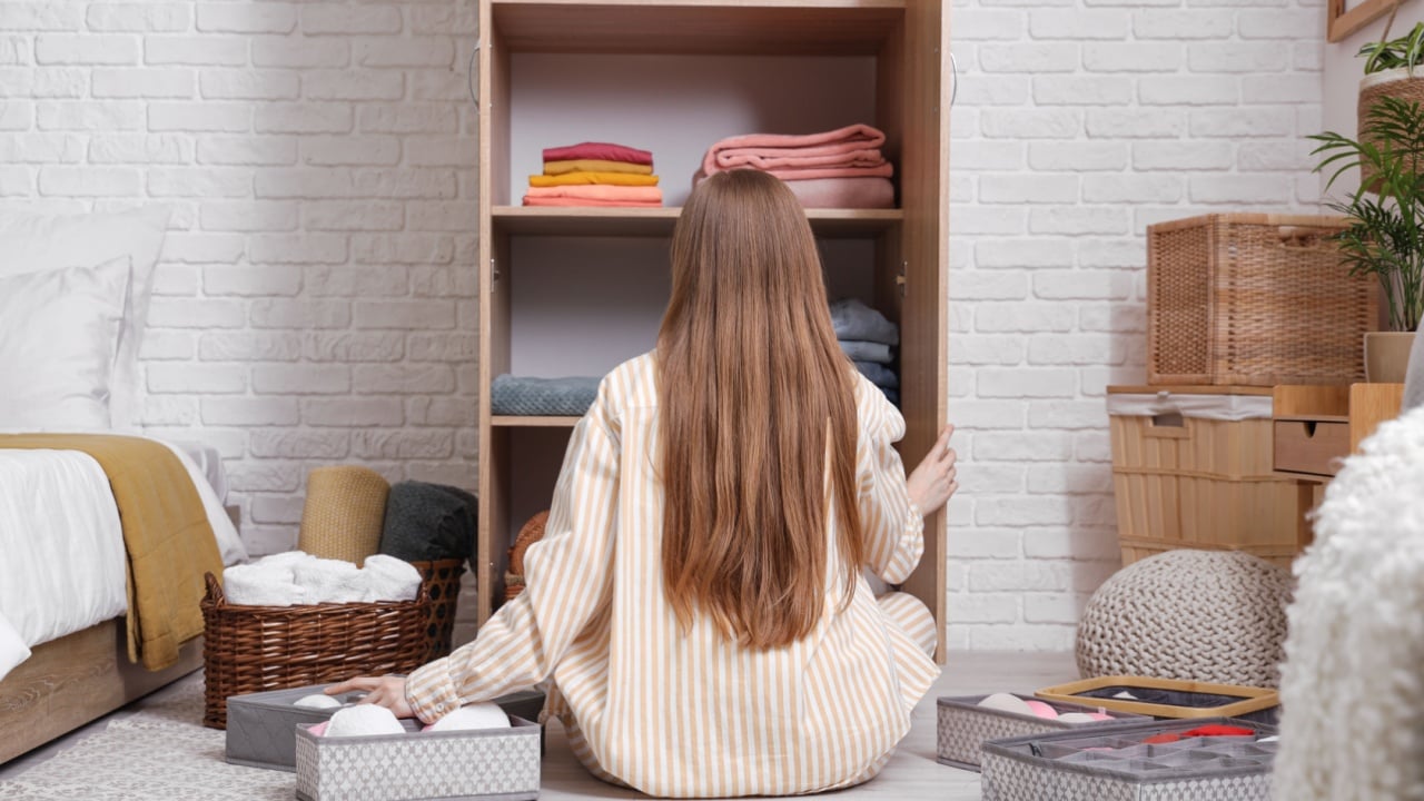 Young woman folding clean clothes in wardrobe