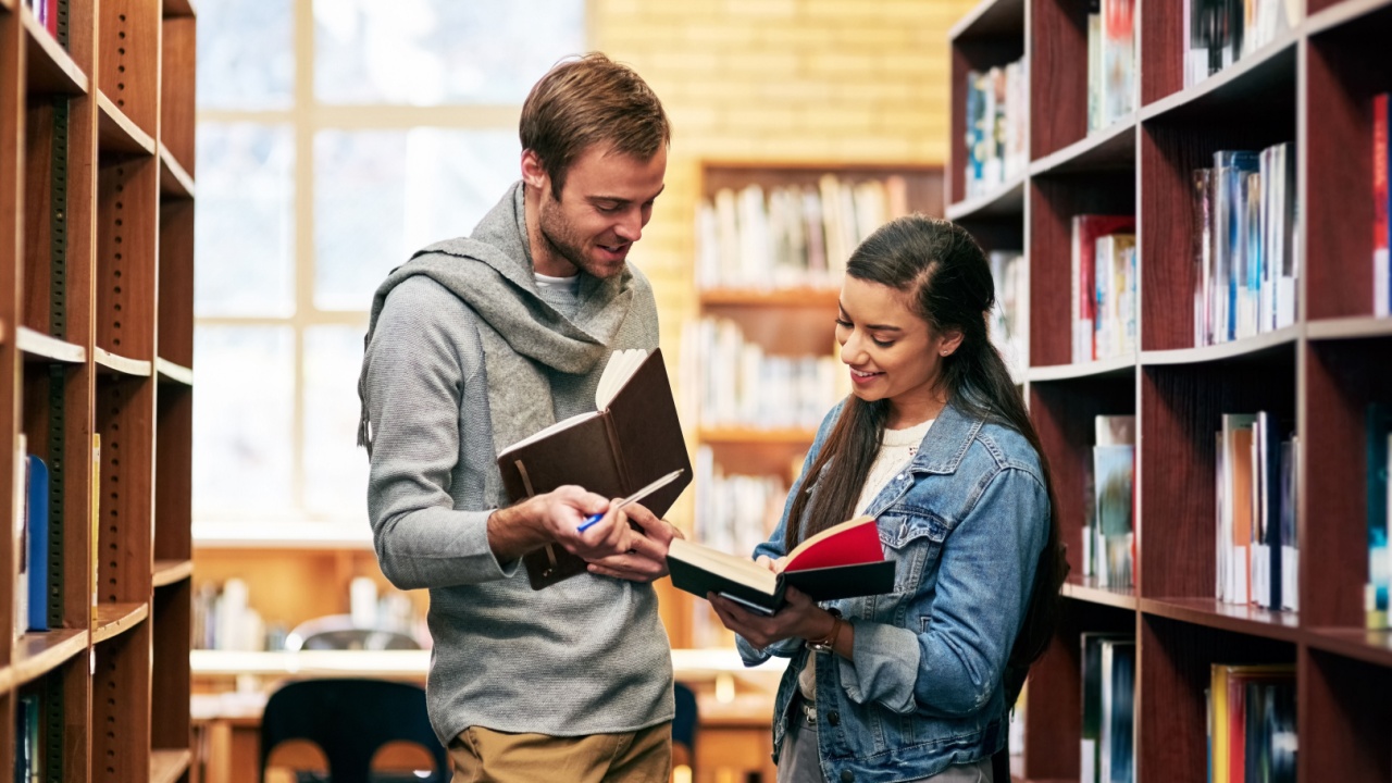 People, students and library conversation with books, happy and campus for learning or university education. Discussion, academic scholarship and collaboration, exam preparation and college thesis