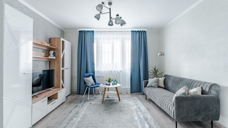 The interior of a small living room in European style apartment . The living room has a wardrobe for storing things , a TV , a coffee table , sofa and an armchair .