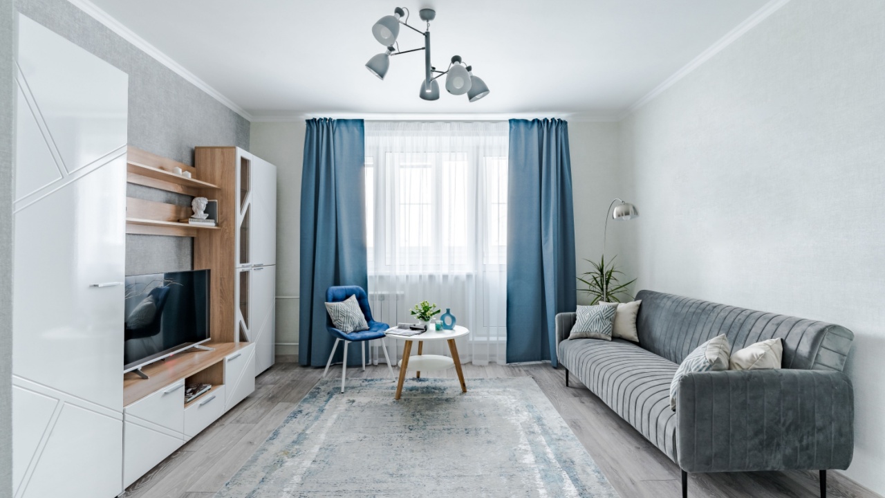 The interior of a small living room in European style apartment . The living room has a wardrobe for storing things , a TV , a coffee table , sofa and an armchair .