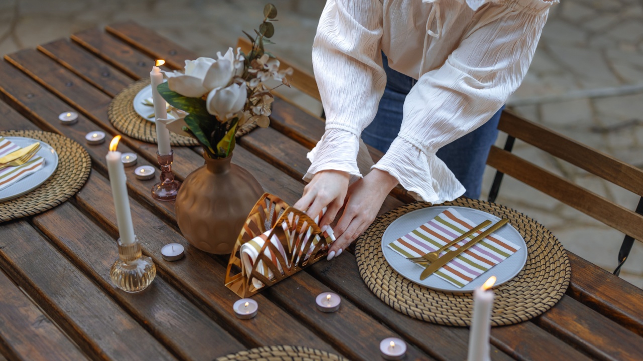 Close up photo of a woman wearing a white shirt arranging napkins on a table set for a private dinner for four with candles.