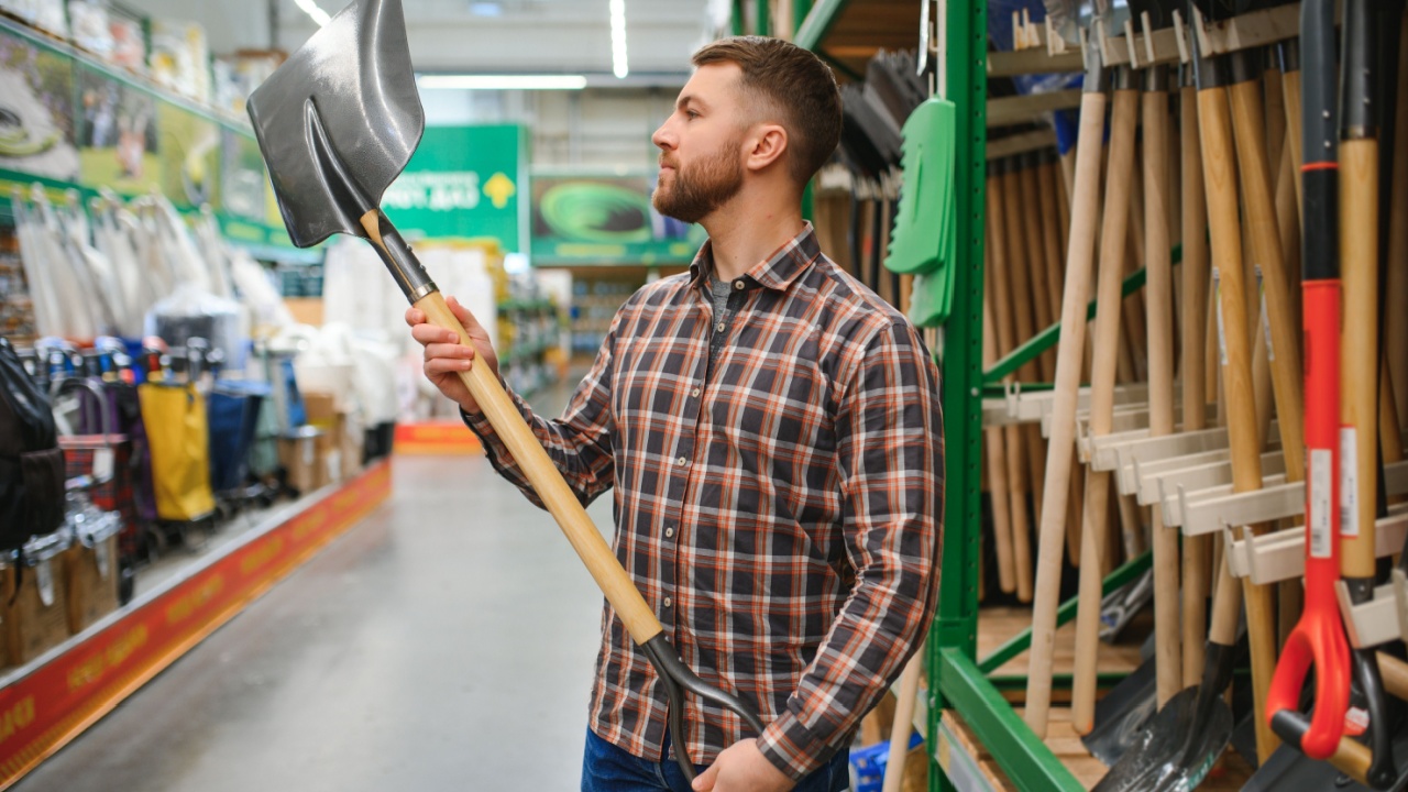 Portrait of a happy young man and customer buying a shovel while shopping at the hardware store.