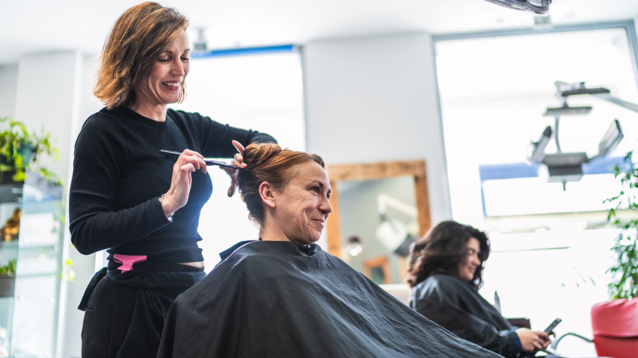 A hairdresser styles a client's hair in a modern salon, creating a neat bun. Concept of professional styling and client satisfaction.