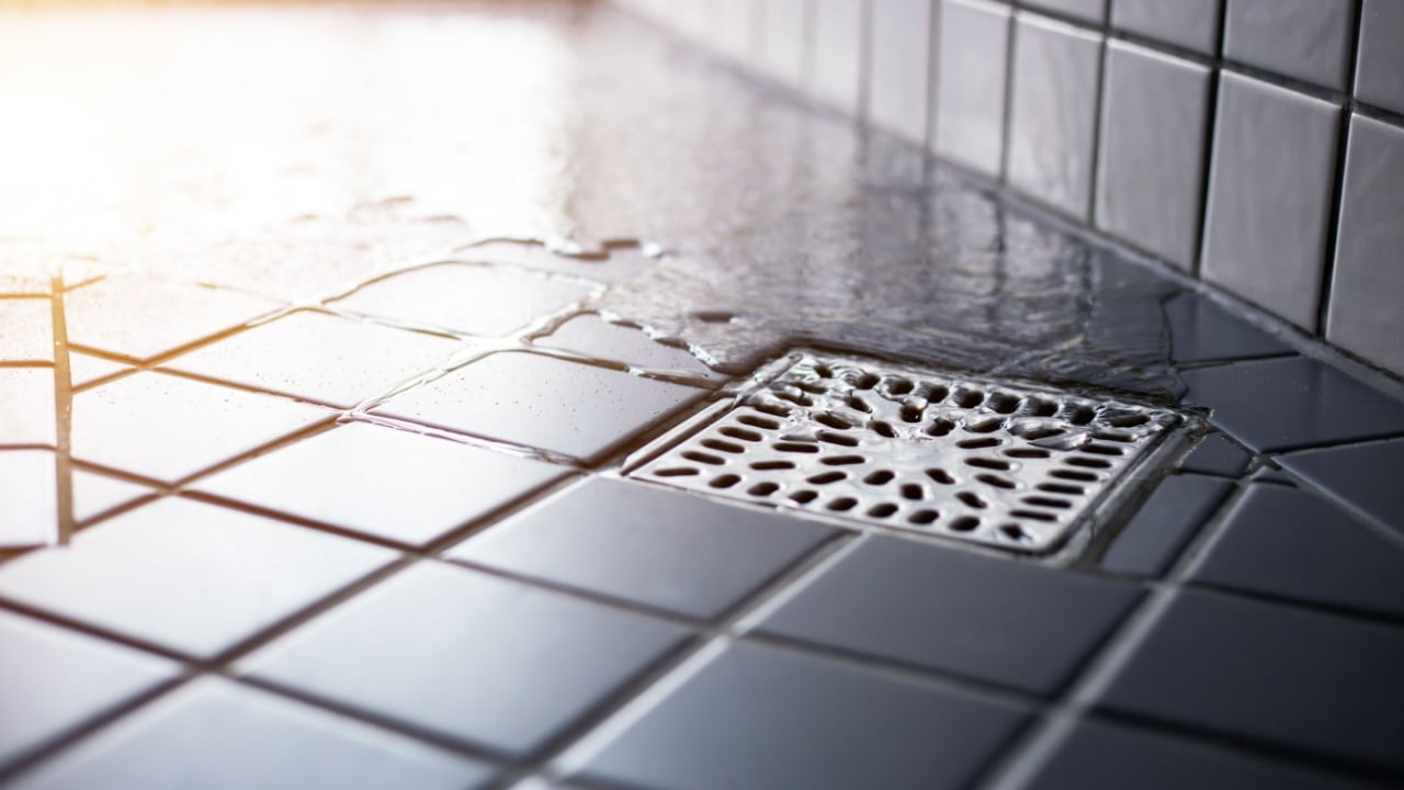 Water flowing to square shower drain hygiene and clean on tiled floor of modern enclosure in bathroom.