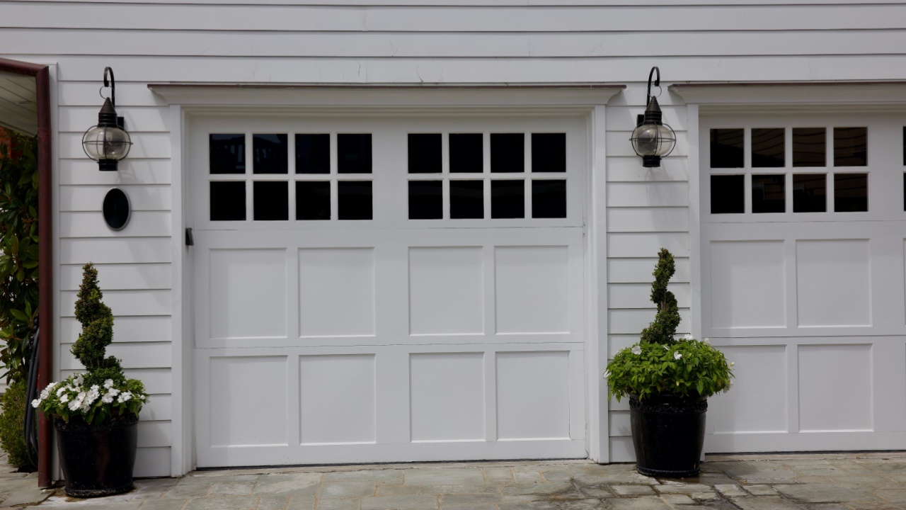 Modern kitchen facade at home with white interior, refrigerator, gas stove appliance, cooking hood, built in oven, sink, water tap, kitchenware supplies on shelves and plants on cupboard furniture