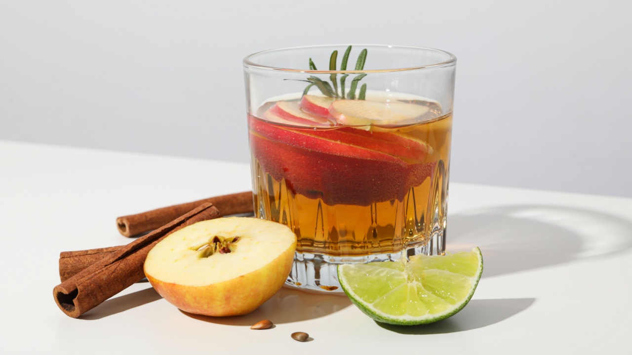 Glass with apple cider, cinnamon sticks, lime and apple pieces on white background, close up