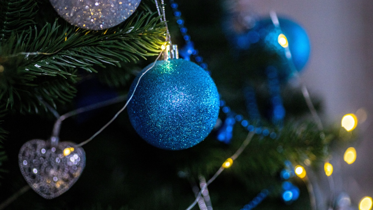 A beautifully decorated Christmas tree features vibrant blue ornaments and sparkling lights, creating a cheerful holiday atmosphere. The shimmering decorations enhance the festive spirit.