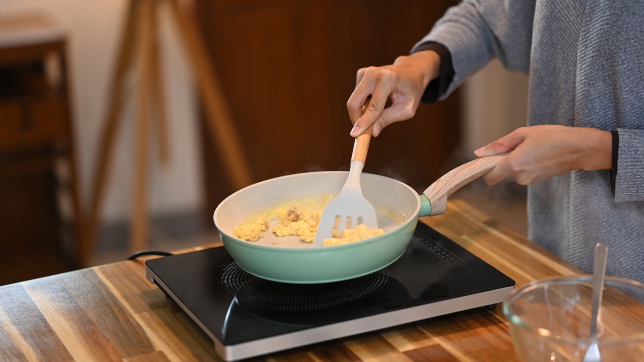 Happy young asian woman preparing scrambled eggs in the kitchen