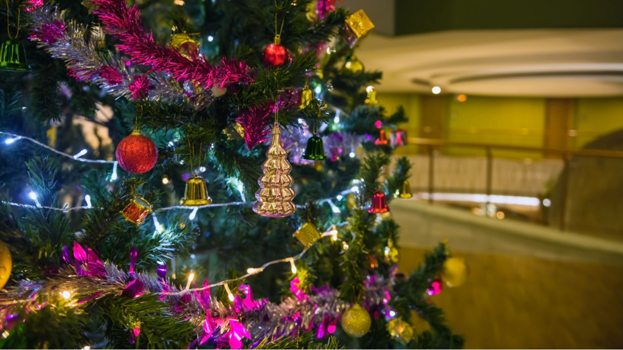 Christmas tree with balls, glowing garland and tinsel on the background of blur modern hotel building at night. Christmas holiday celebration.