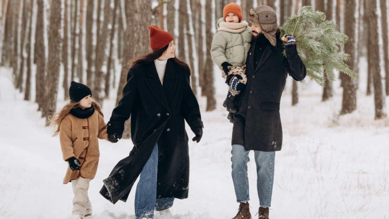 Winter holidays and people concept - happy family with little daughters choosing Xmas tree at forest. Happy preparation for the celebration of New Year holidays, family portrait on the walk