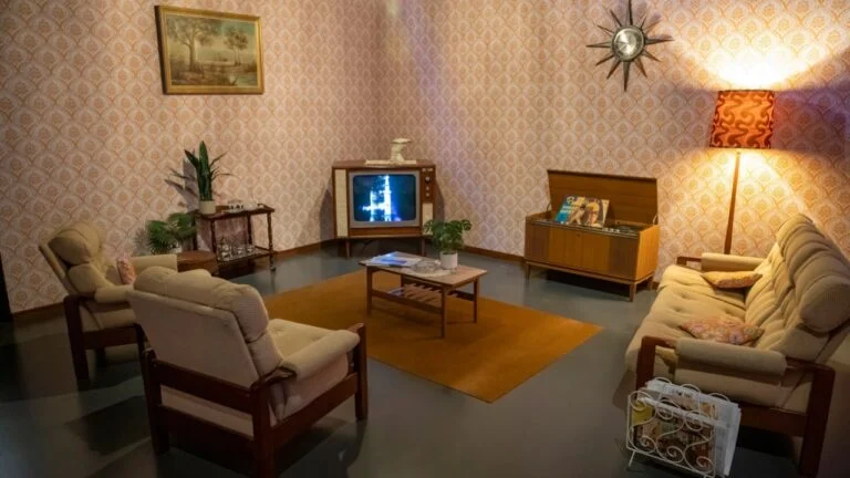 Perth Australia 2024-03-18 A vintage-style living room featuring 1970s decor with retro furniture, patterned wallpaper, a television displaying a rocket launch.