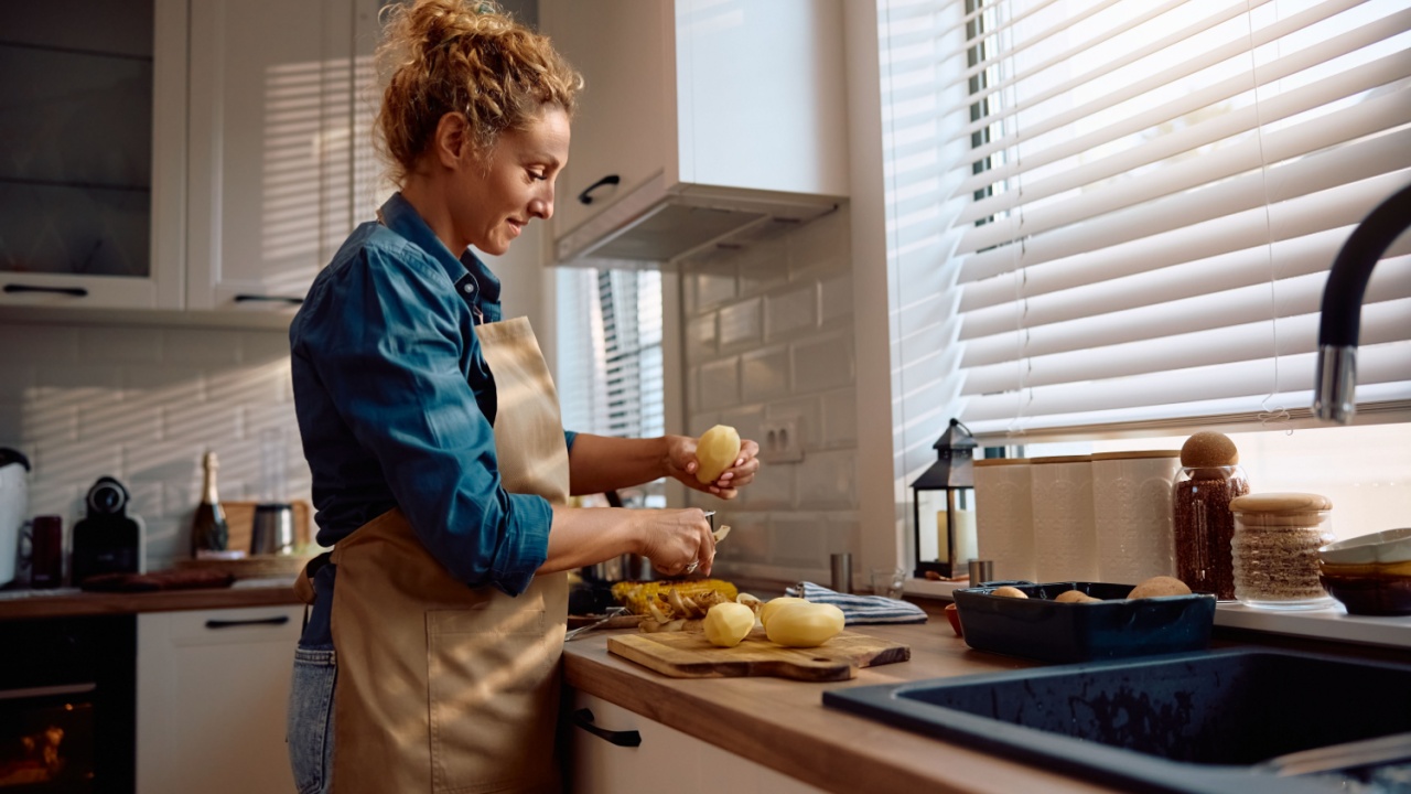Smiling woman peeling potatoes while cooking for Thanksgiving at home. Copy space.