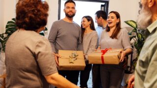 A mature couple greets their smiling guests at home. Laughing adult children came to their parents with gifts. Happy people spend family holidays together. Modern cozy home interior.