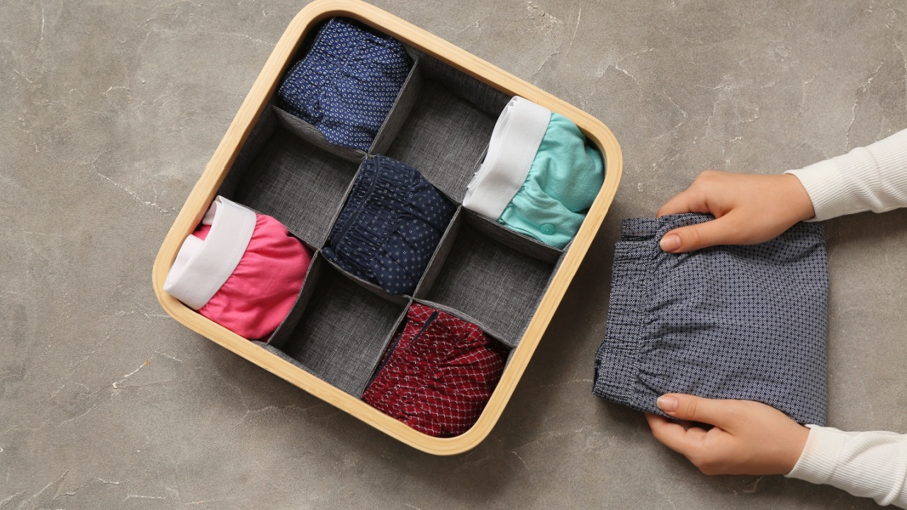 Woman putting folded male trunks into organizer on grey grunge background