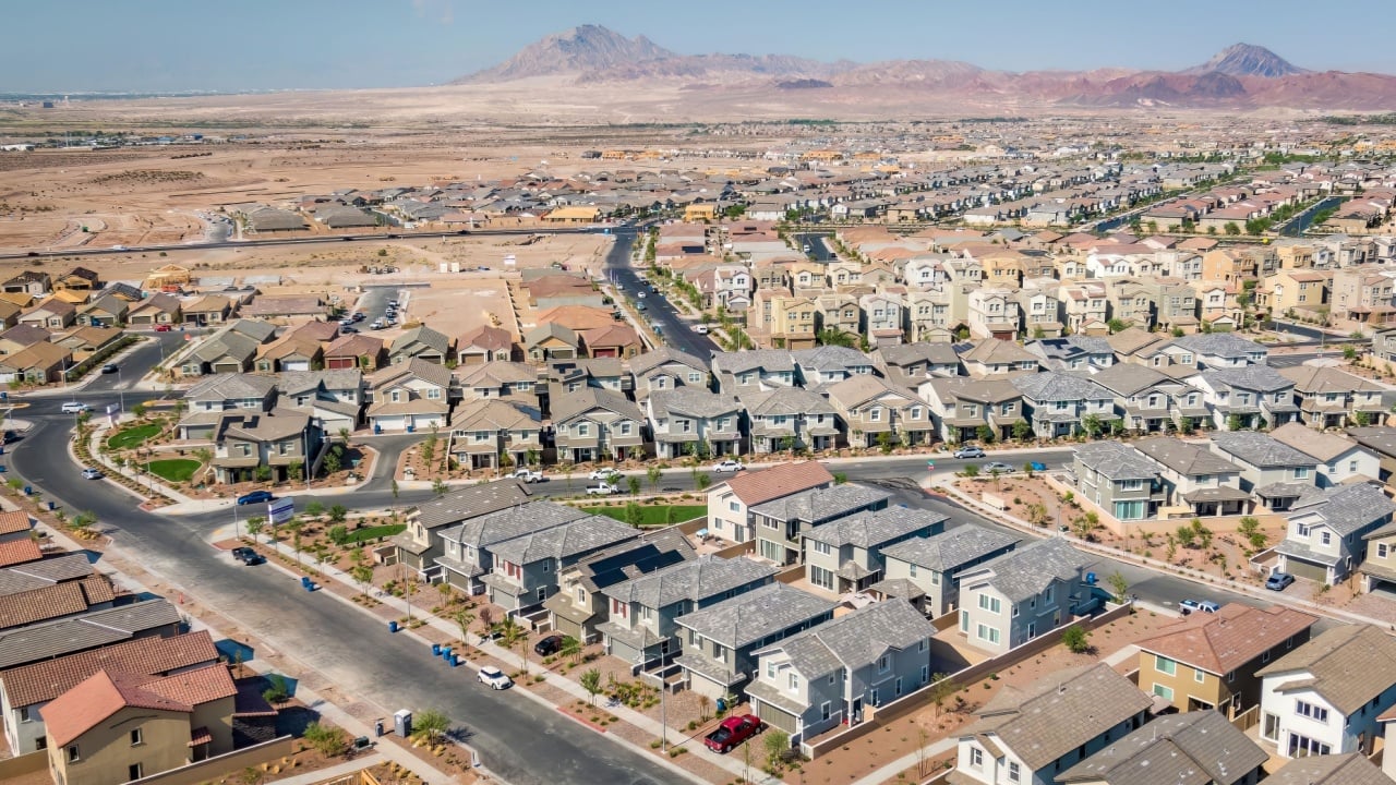 Aerial view captures the sprawling residential area of Henderson, Las Vegas, Nevada, featuring newly built homes with desert mountains in the background on a sunny day