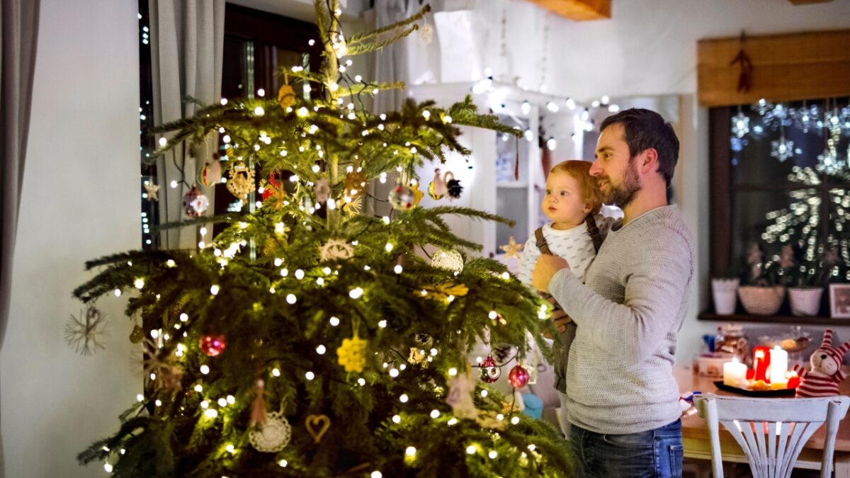 Father showing christmas tree to little son in Christmas home. Cute baby boy is amazed by christmas decorations.