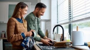 Cheerful man having fun while doing the dishes with his wife at home.