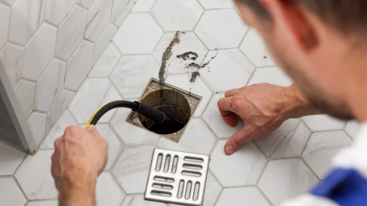 plumber unclogging blocked shower drain with hydro jetting at home bathroom. sewer cleaning service