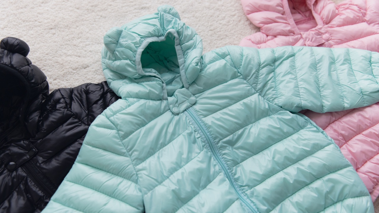 Mint, pink, orange, and black ultra-light down jackets for kids, featuring cute bear ears on the hood, displayed on a soft, white fur carpet