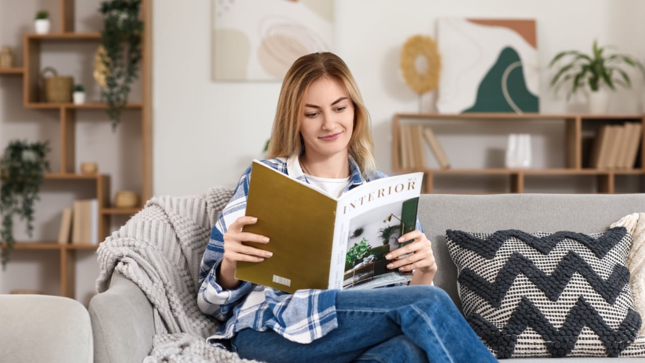 Young woman reading magazine on sofa at home