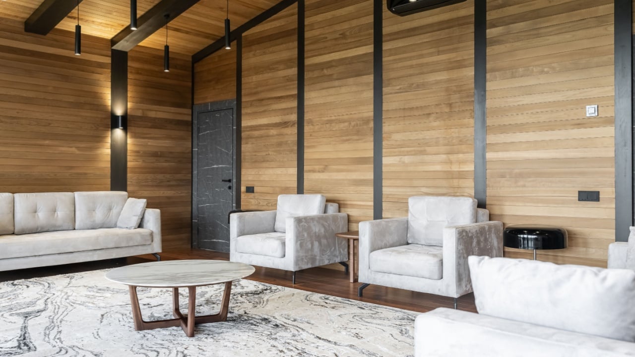 stylish living room with grey armchairs, round table, carpet, TV. Wooden walls. modern room with matching furniture theme set. Elegant interiors with chic and minimalist interior design elements.