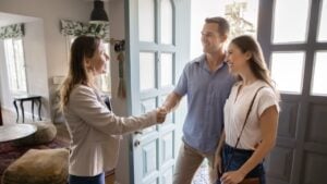 Successful female real estate insurance agent and couple of customers shaking hands at home. Homeowners, property buyers, renters consulting realtor in apartment, giving handshake