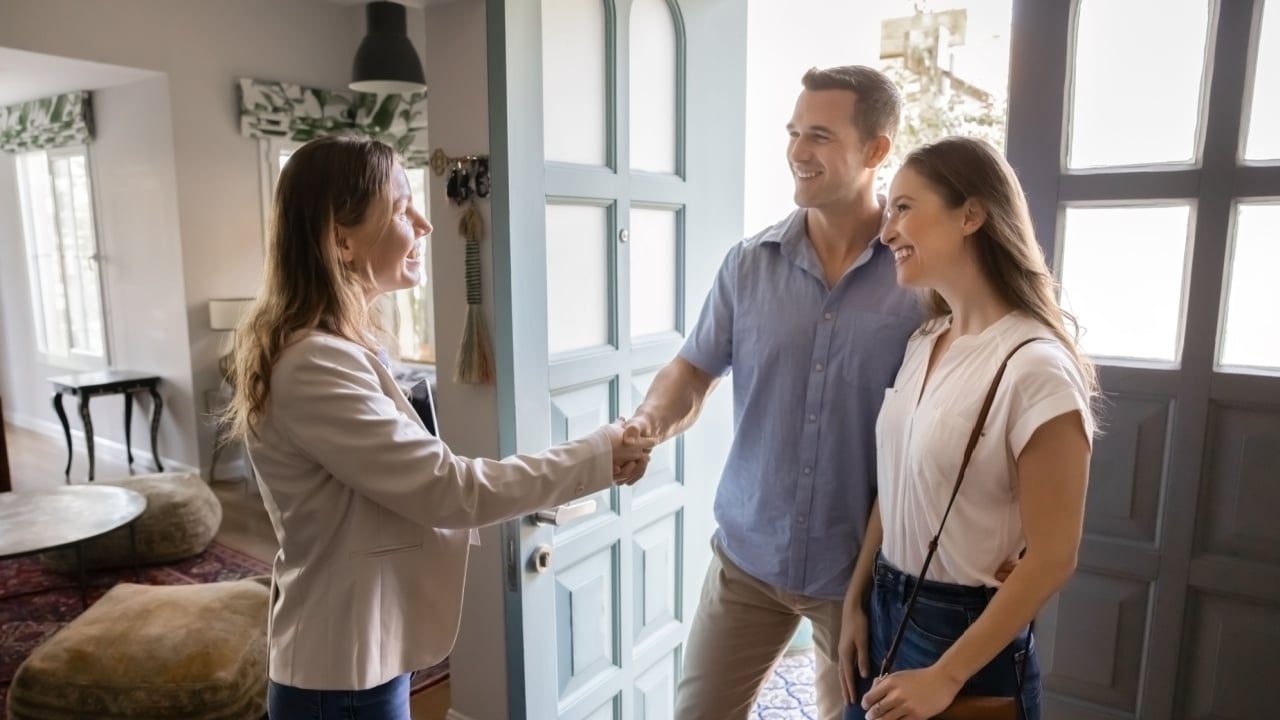 Successful female real estate insurance agent and couple of customers shaking hands at home. Homeowners, property buyers, renters consulting realtor in apartment, giving handshake